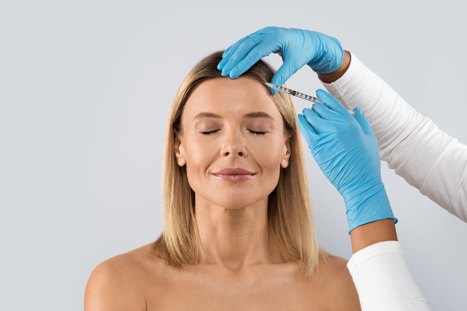 A person receives a cosmetic forehead injection from a medical professional wearing blue gloves.