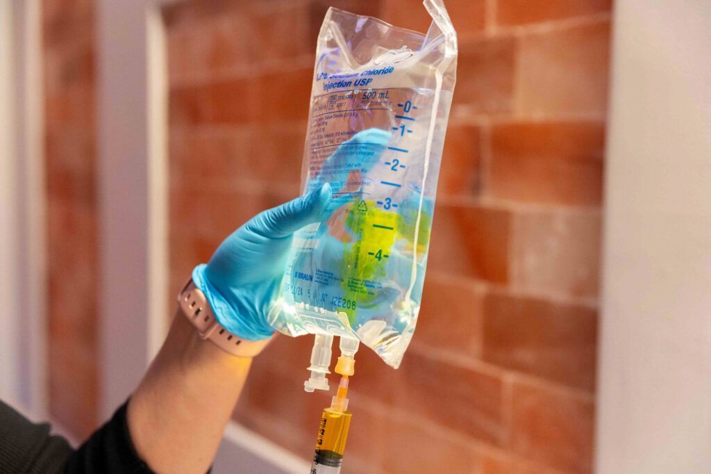 A person is holding a bag of liquid with a syringe attached to it.