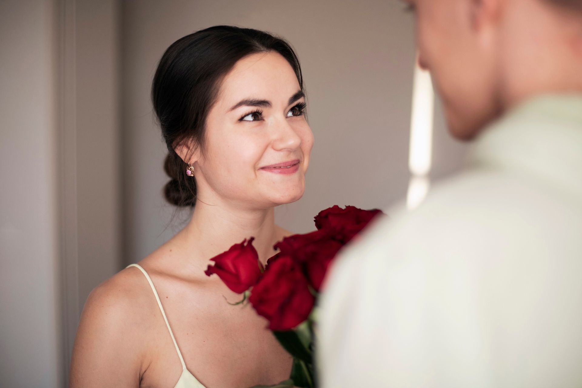 Woman smiles at a person, holding red roses, in a well-lit room.
