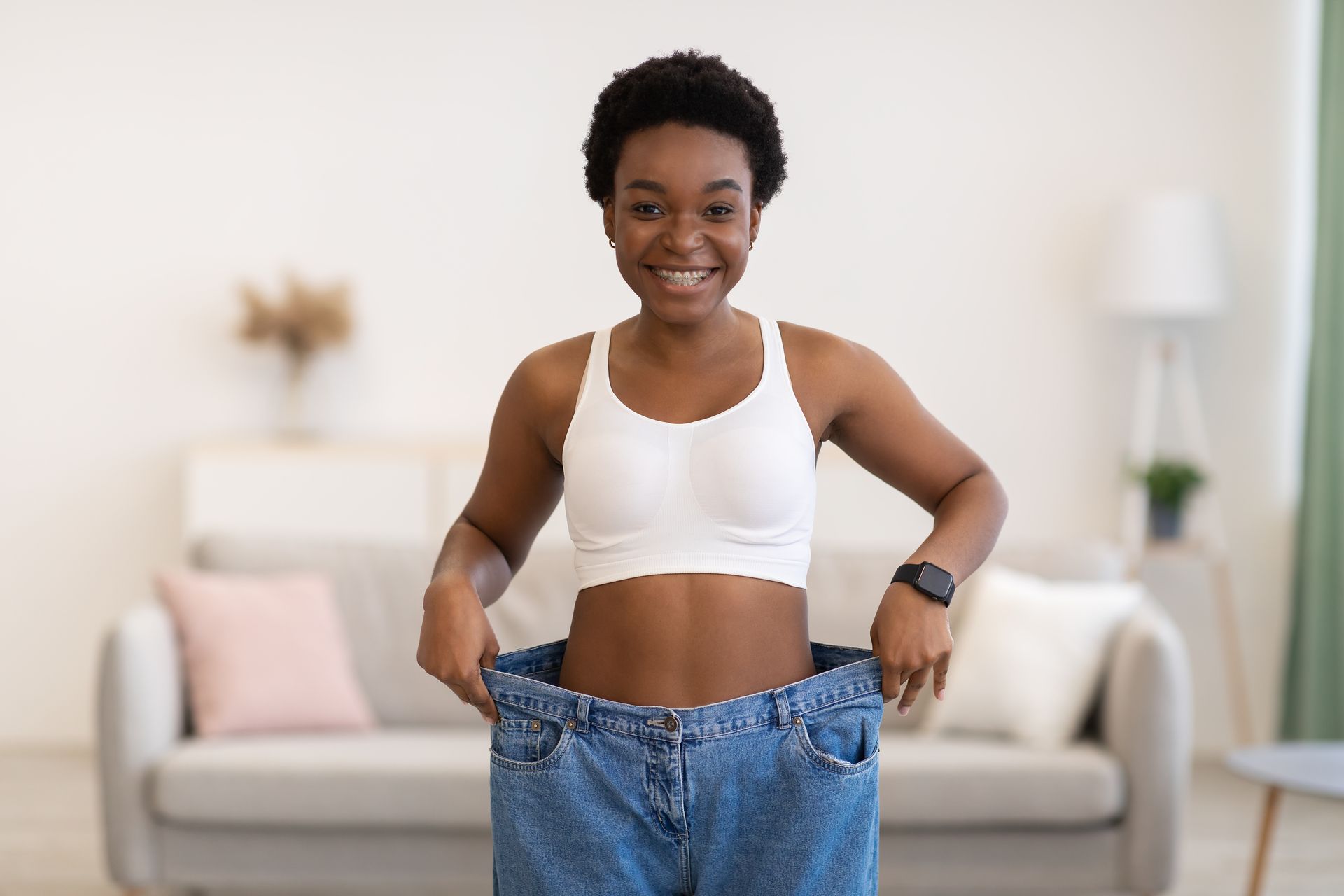 A woman is standing in a living room wearing a pair of oversized jeans.