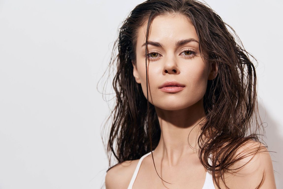 A woman with wet hair is wearing a white tank top and looking at the camera.