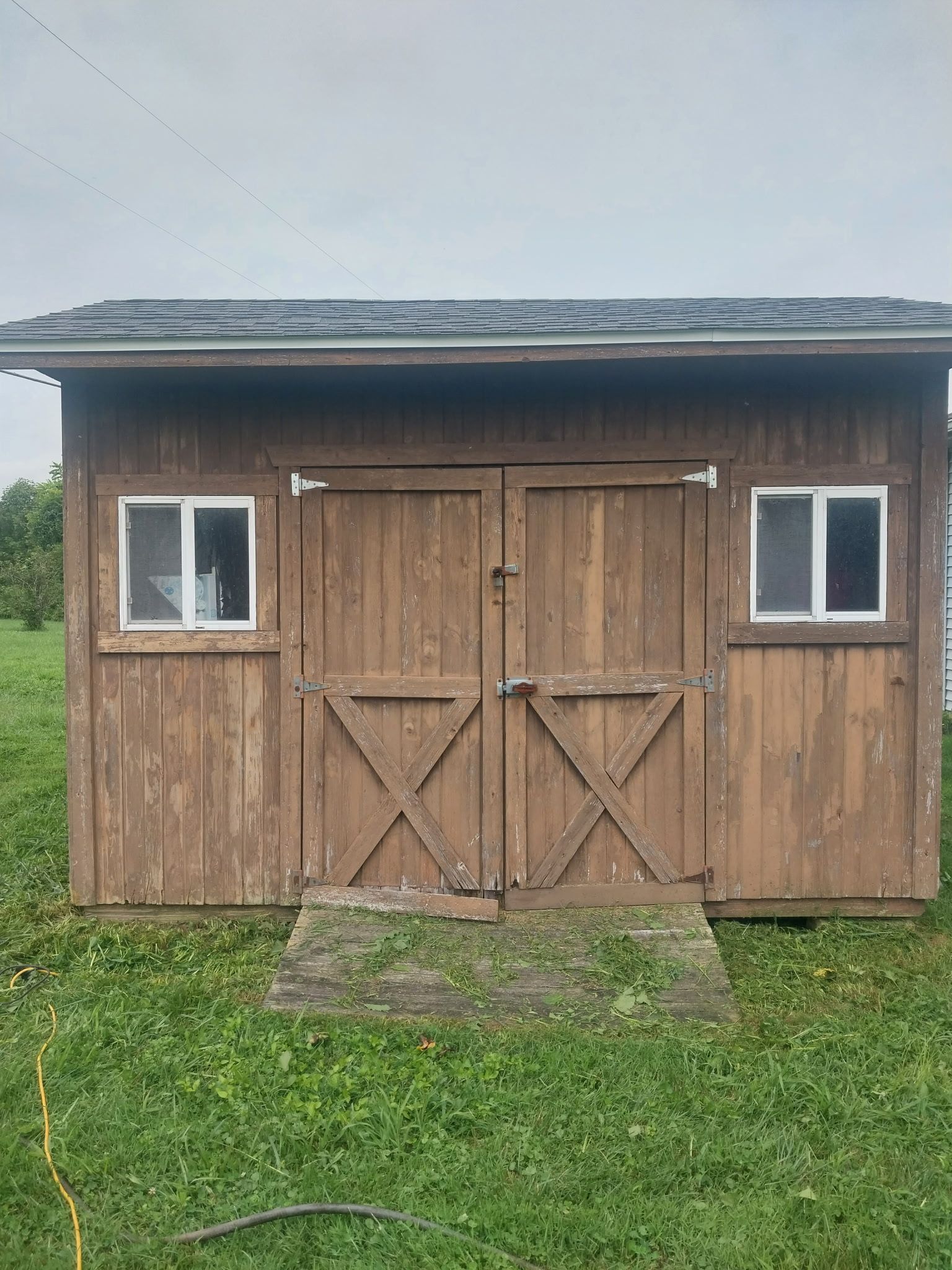 Brown shed with double doors, two windows, and a small ramp on a grassy field.