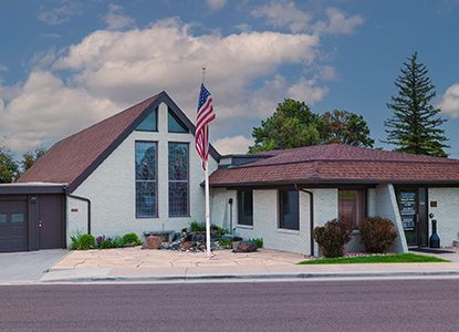 Church building with brown roof, American flag, and landscaping.