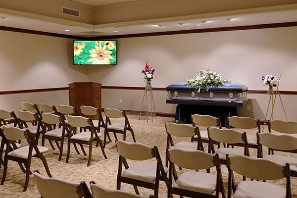 Funeral home interior with casket, chairs, and floral decorations.