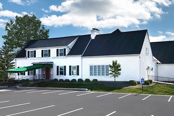 White building with black roof, green awning, parking lot, and a blue handicap sign.