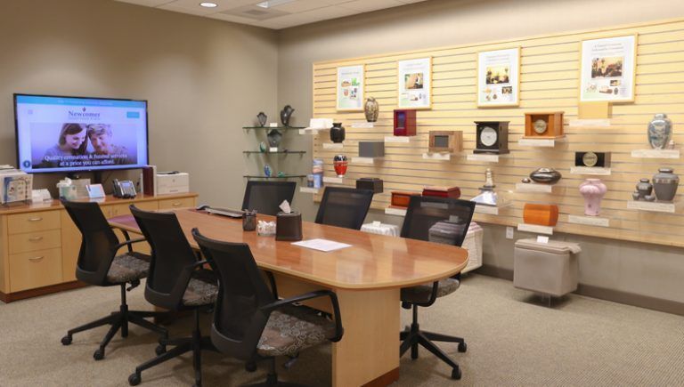 A funeral home conference room with a display of urns and a screen showing a video.