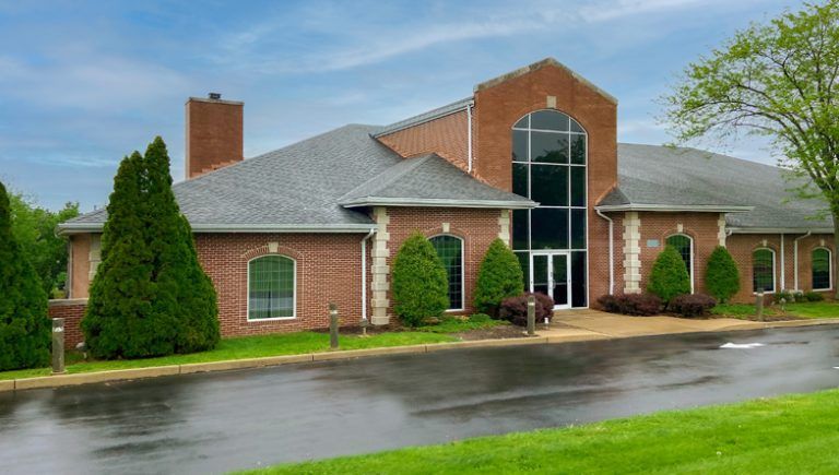 Red brick building with a tall, arched window and several smaller windows. A wet road and green lawn in the foreground.