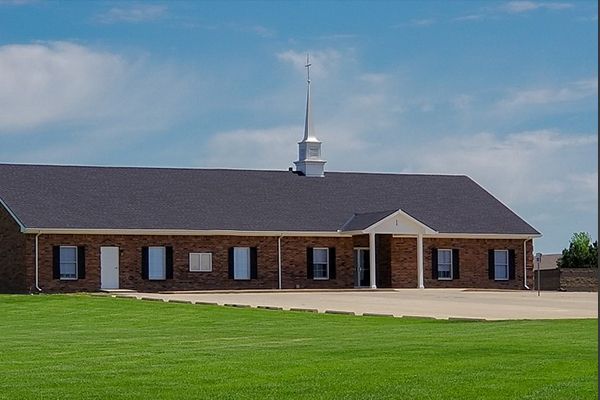 Brick church with dark roof, steeple, and lawn on a sunny day.
