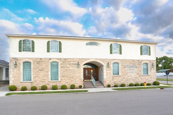 Two-story brick building with green shutters, arched doorway, and manicured lawn.