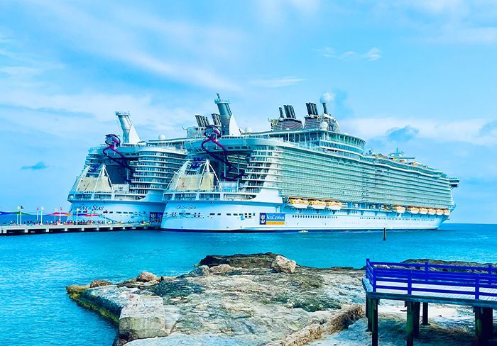 Two large cruise ships docked at a pier on a bright, sunny day. Turquoise water and blue sky.