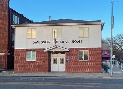 Davidson Funeral Home exterior, red brick and white facade, double doors, accessible entrance, flag, and street view.
