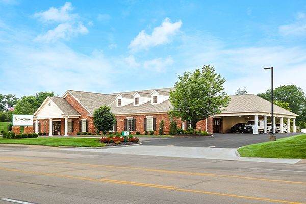 Brick building with a sign that says “New Visions,” blue sky, green grass, and small trees.