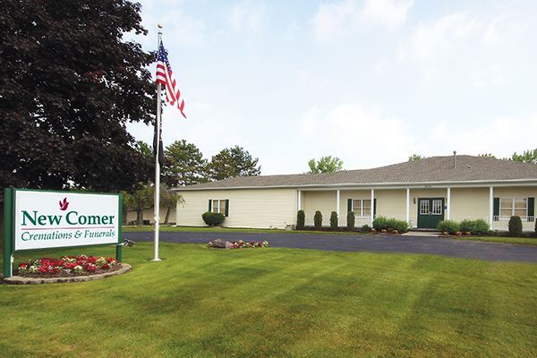 New Comer funeral home, a single-story building with a sign, lawn, and American flag.