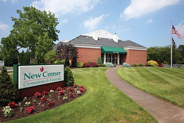 New Comer Cremations & Funerals building with green sign, brick exterior, and American flag.