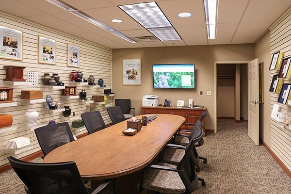Funeral home consultation room with urns, pictures, and a computer on a conference table.