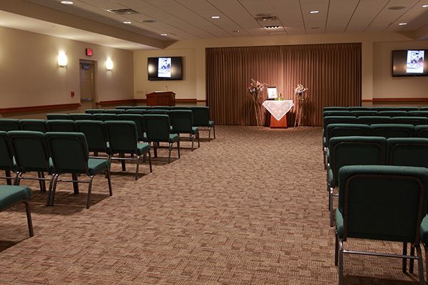 Rows of green chairs face a stage with a brown curtain, likely a memorial service.