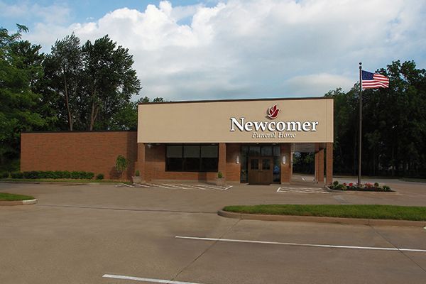 Newcomer Funeral Home building with red brick and tan facade, American flag, and parking lot.