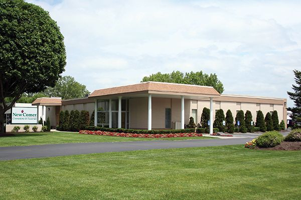 A beige one-story funeral home with a green lawn, trees, and a sign.