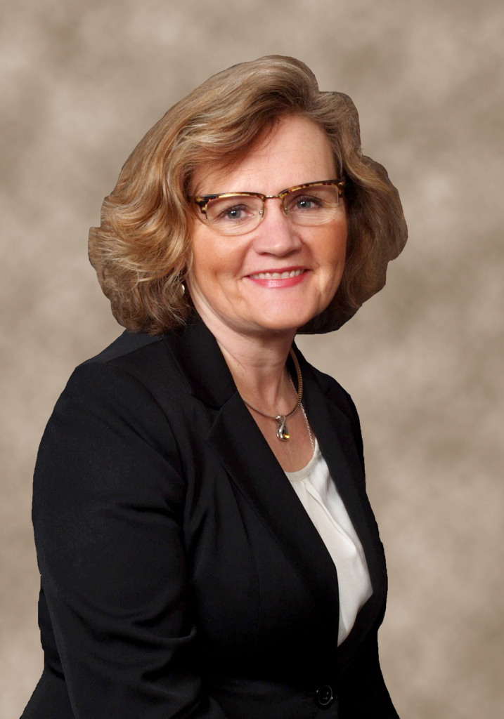 Woman with glasses, smiling, in a black blazer and white shirt. Posed portrait against a brown background.