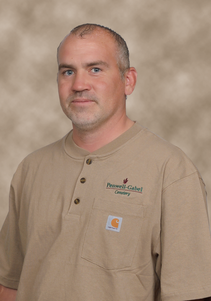 Man in tan work shirt with logo, smiling slightly.
