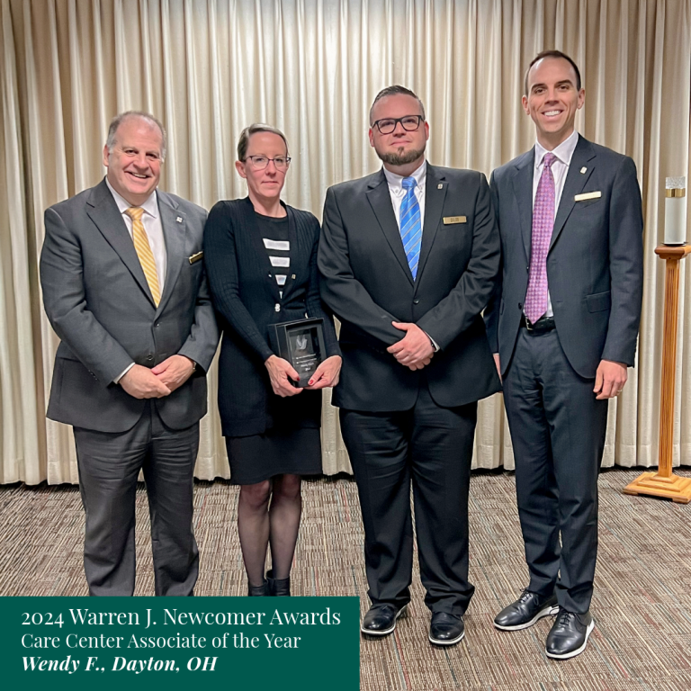 Four people in suits at an awards ceremony. Wendy F. holds a plaque. Text reads