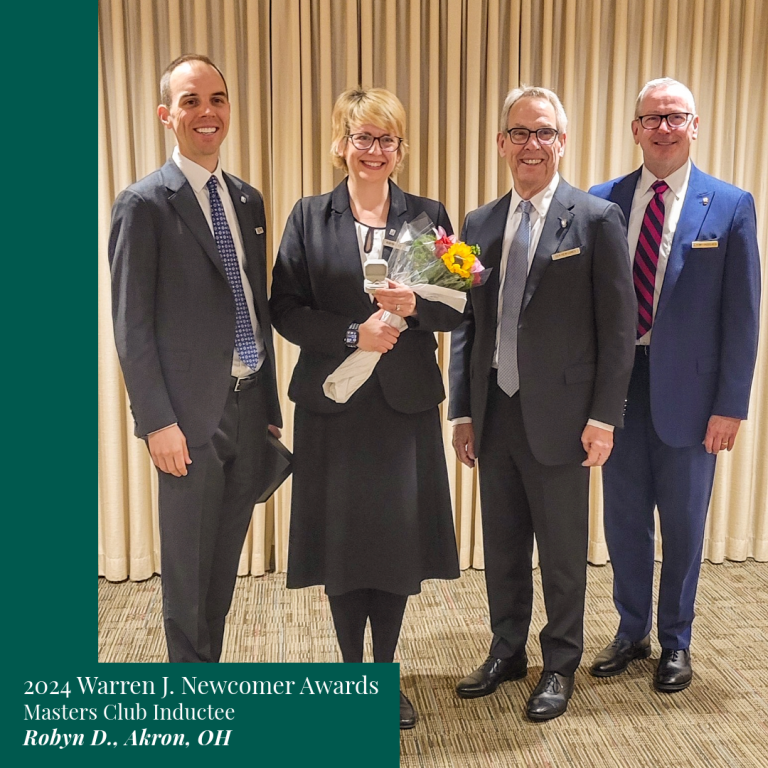Four formally dressed people at an event. Woman holds flowers. Others smile.