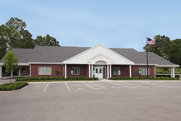 A brick building with white trim and a gray roof; parking lot in front. An American flag flies on the right.