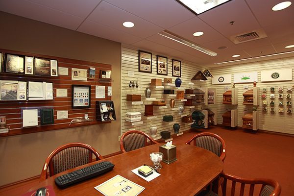 A funeral home consultation room with display of urns and keepsakes, centered around a wooden table and chairs.