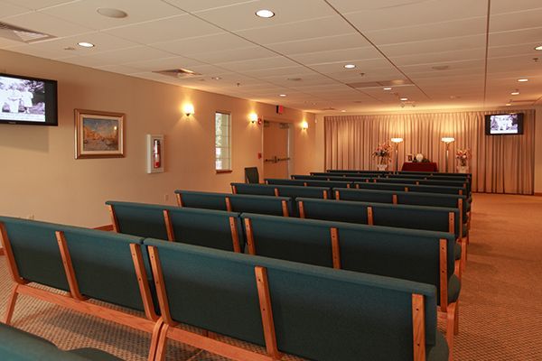Empty funeral home chapel with green benches, beige walls, and curtains.