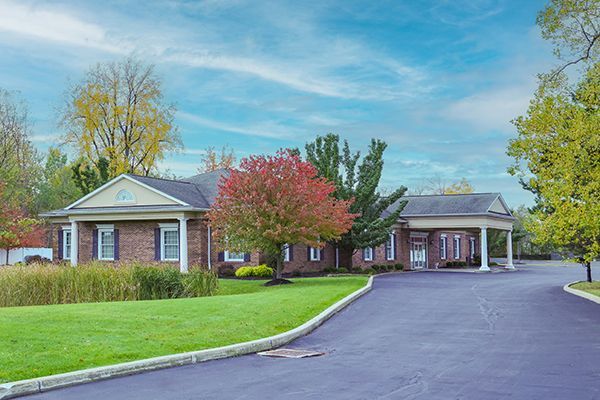 Brick building with a long driveway; trees with fall foliage, green lawn, and blue sky.
