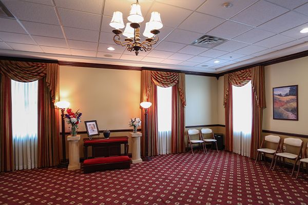 Formal room with red carpet, beige walls, and chairs; funeral home setting.
