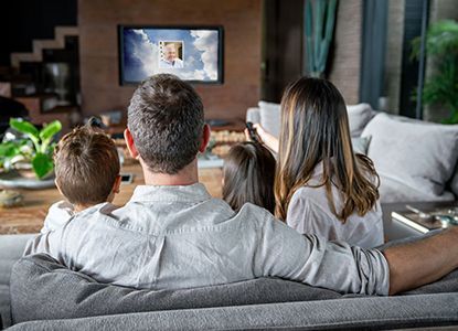 Family watching TV together on a couch; sunny scene displayed on the screen.