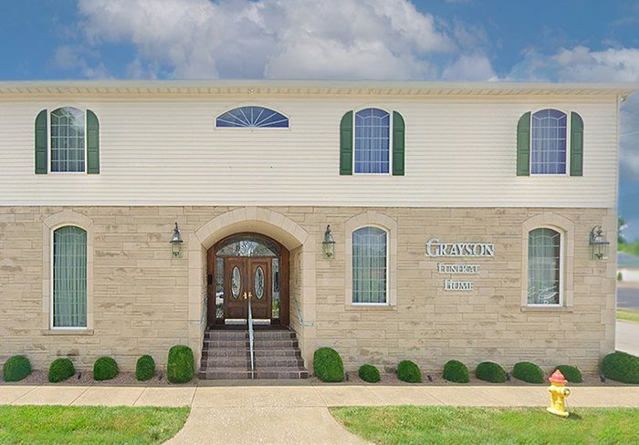 Two-story building with stone and beige siding. Arched entrance, windows with green shutters, and Genesis sign.
