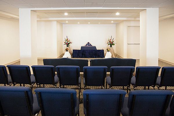 Blue chairs face a raised stage with flowers in a funeral home.
