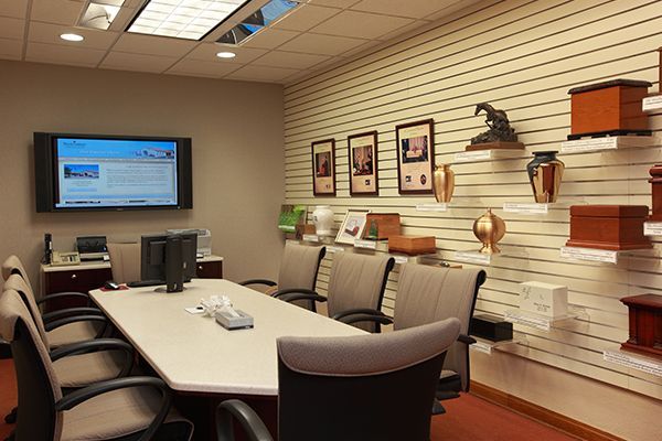 Meeting room with a large screen, table, chairs, and urns displayed on the wall.