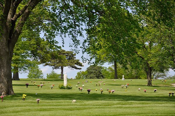 Lush green cemetery lawn dotted with headstones under a canopy of trees.