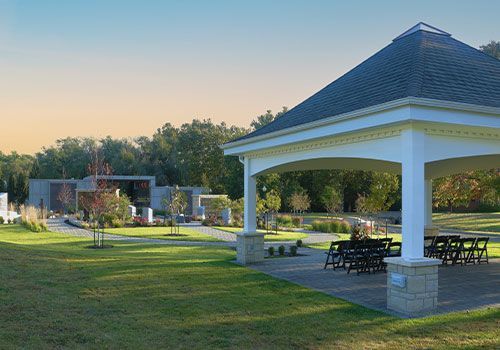 Lawn with gazebo, tables/chairs, and modern building in distance, under a blue sky with sun.