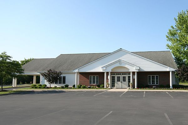 A one-story brick building with a white gable entrance and a parking lot on a sunny day.