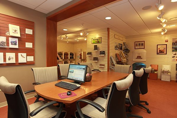 Conference room with large wooden table, computer, and chairs. Display area in the background.