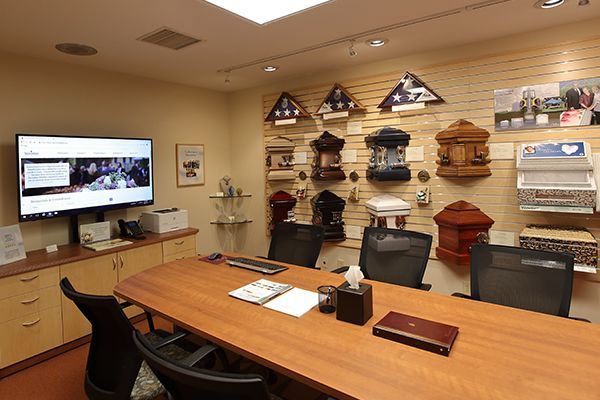 A funeral home conference room with urns and caskets on display, along with a TV, table, and chairs.