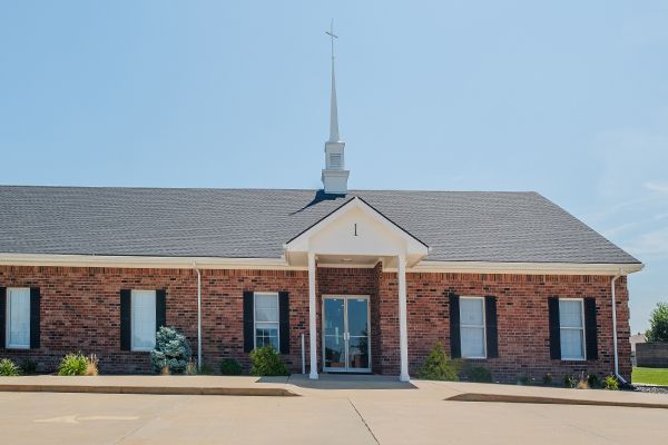 Brick church building with a tall steeple against a clear blue sky.