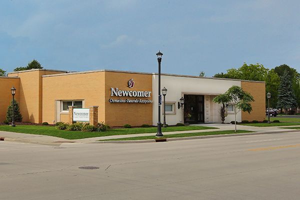 Exterior view of the Newcomer Funeral Home building; tan and white brick with green landscaping and street lamps.