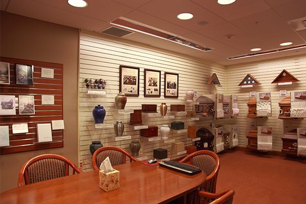 A funeral home consultation room with urns, photos, a table, and chairs.