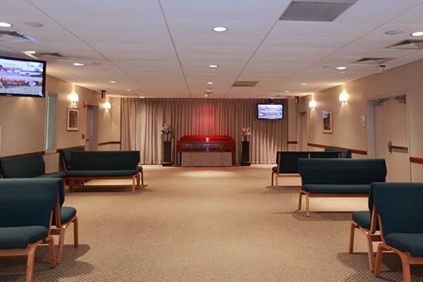 A funeral home chapel with blue seating, altar, and two TVs on the walls.