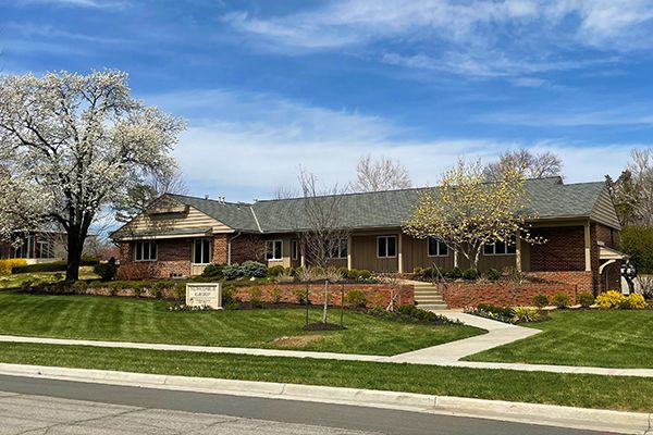 A single-story brick and beige house with a manicured lawn and blooming trees under a blue sky.
