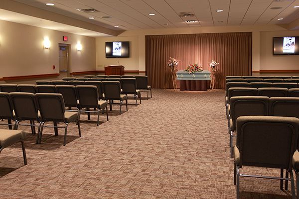 Empty funeral home with rows of chairs facing a stage with a curtain and flowers.