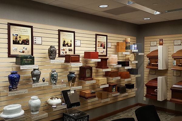 Funeral home display: Urns, caskets, and framed displays on a slat wall, various colors, indoors.