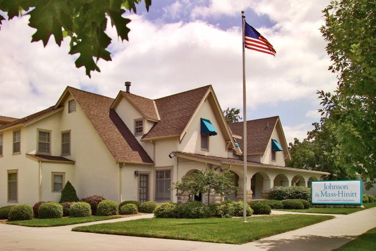 Johnson Mortuary building with flag, blue awnings, and green lawn.