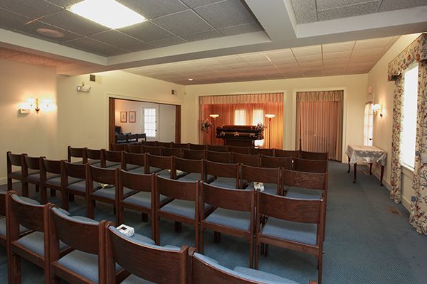 Rows of wooden chairs face a piano and stage in a funeral home chapel.