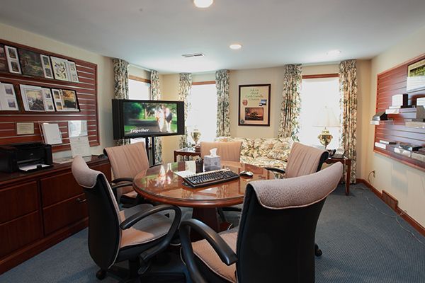 Office meeting room with round table, chairs, TV, couch, and windows.